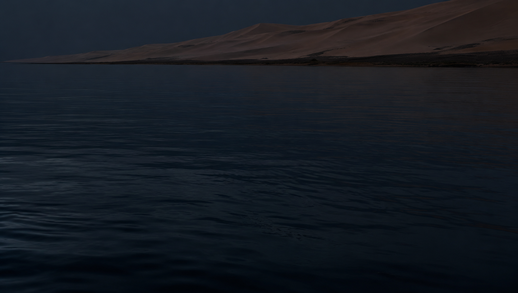 Sand dunes meeting deep blue water at dusk